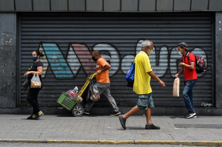 People walk past the metal gate of a closed shop reading "Maduro" in Caracas amid the COVID-19 pandemic, on September 3, 2020 as inflation increases in Venezuela which is in the midst of the worst economic crisis in its history after years of recession