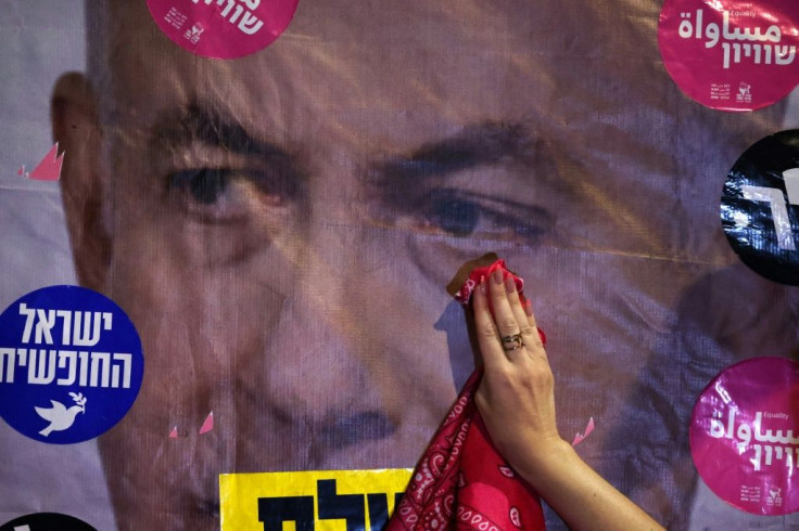 An Israeli protester mimics wiping a tear off a poster depicting Prime Minister Benjamin Netanyahu during a demonstration against him in front of his residence in Jerusalem on June 12