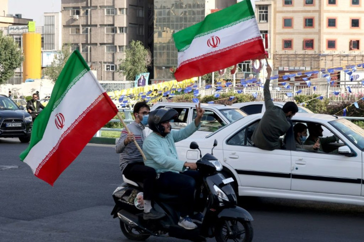 Iranians waving national flags drive past an electoral banner showcasing Iran's ultraconservative candidate Ebrahim Raisi during a street rally in the capital Tehran on June 15, 2021