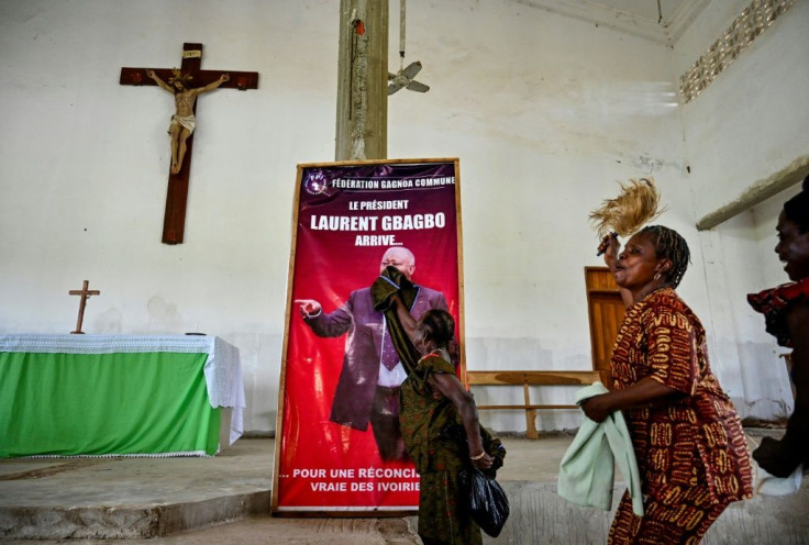 A woman dusts a poster reading 'President Laurent Gbagbo arrives for a true reconciliation of Ivorians' before a mass in his hometown of Mama