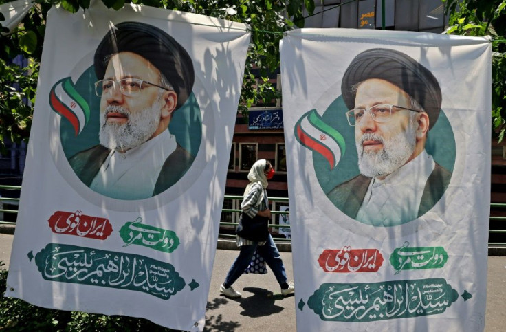 A woman walks past banners of presidential election favourite Ebrahim Raisi on the eve of polling day in Tehran