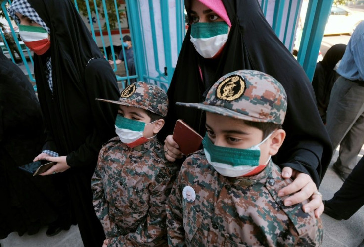 An Iranian woman queues to vote in Tehran, accompanied by her sons wearing Revolutionary Guard uniforms