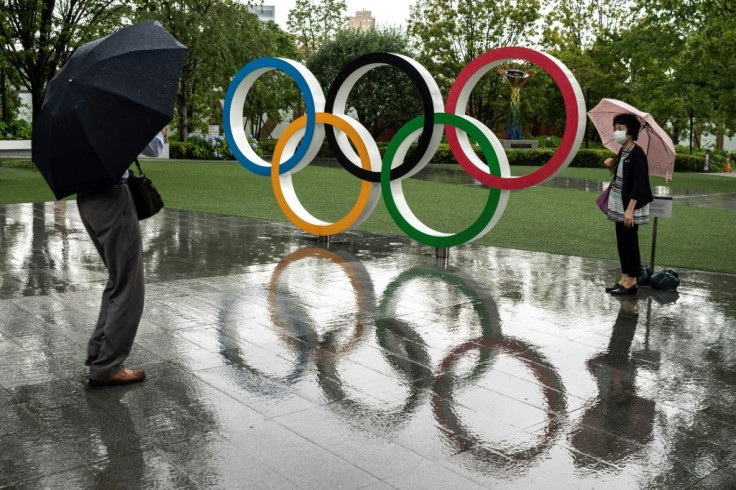 Rail falls as people walk past the Olympic rings near the National Stadium, main venue for the Tokyo 2020 Games, on June 23, 2021