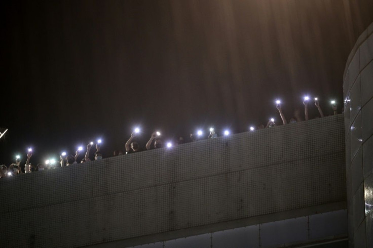 Employees of the Apple Daily newspaper shine phone torches from their office rooftop during heavy rain and shout thanks to supporters down on the street below in Hong Kong on June 23, 2021