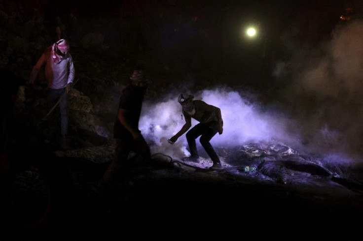 A Palestinian protester throws back a tear gas canister fired by Israeli soldiers during nighttime clashes