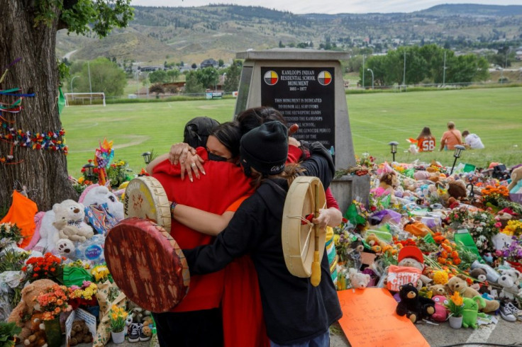 People from Mosakahiken Cree Nation hug in front of a makeshift memorial at the former Kamloops Indian Residential School to honour the 215 children whose remains have been discovered buried near the facility, in Kamloops, British Columbia, Canada, on Jun