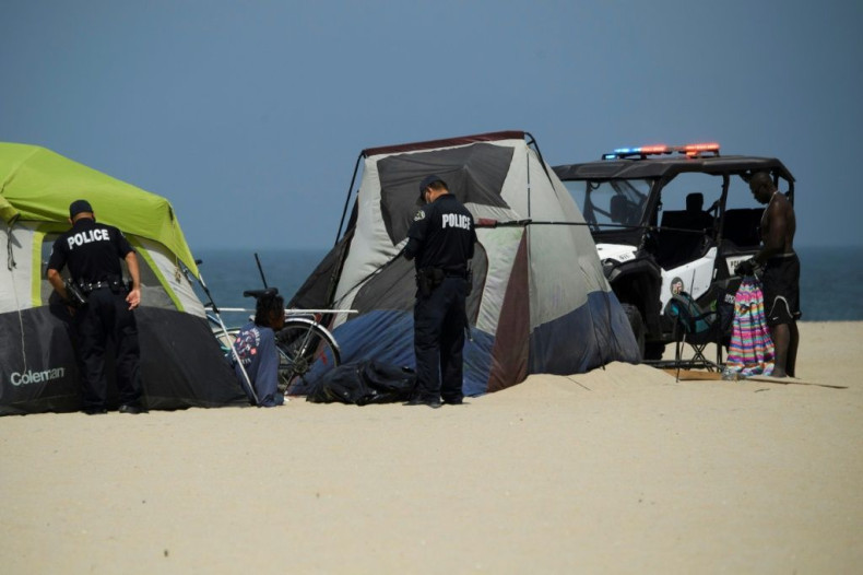 Los Angeles police inspect an encampment at Venice Beach on June 16, 2021 where Rodrick Mims, 50, (R) who has been homeless off and on over the last 15 years, is living by the Pacific Ocean