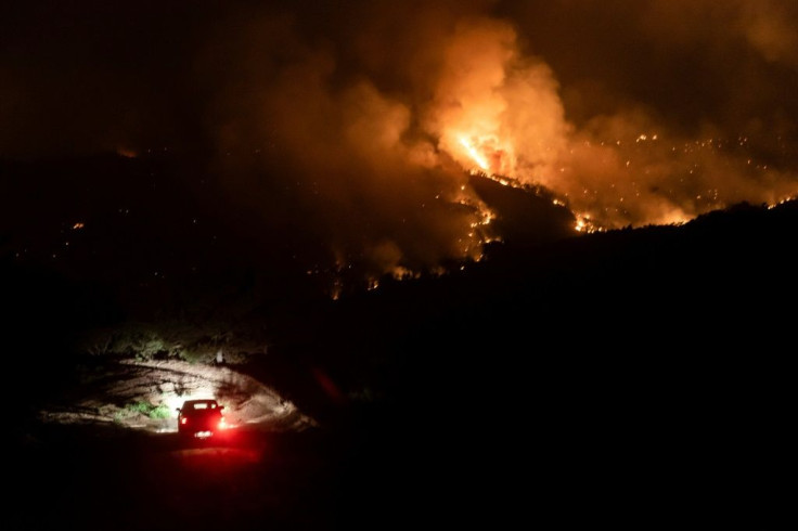 A car drives on a road in the village of Vavatsinia in the Larnaca district of Cyprus as a giant wildfire rages on the hills above during the night of July 3