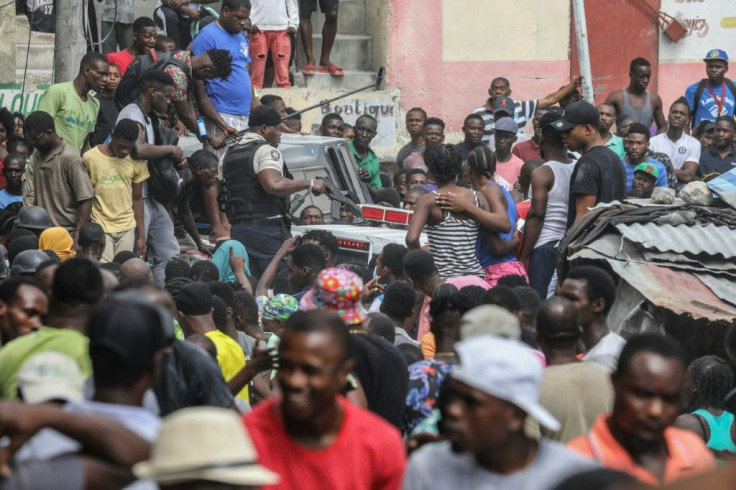 Crowds watch as two men, accused of being involved in the assassination of President Jovenel Moise, are transported to the Petionville station in a police car in Port-au-Prince