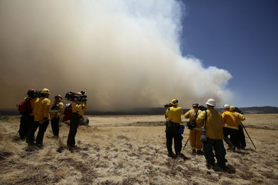 Reporters stand in a field as they watch smoke billowing over the White Mountains from the Wallow Wildfire in Apache County, Arizona