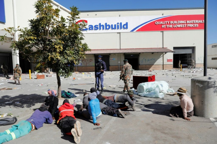 South African troops patrol the the ransacked Diepkloof Square shopping mall in Soweto as suspected looters lie on the ground
