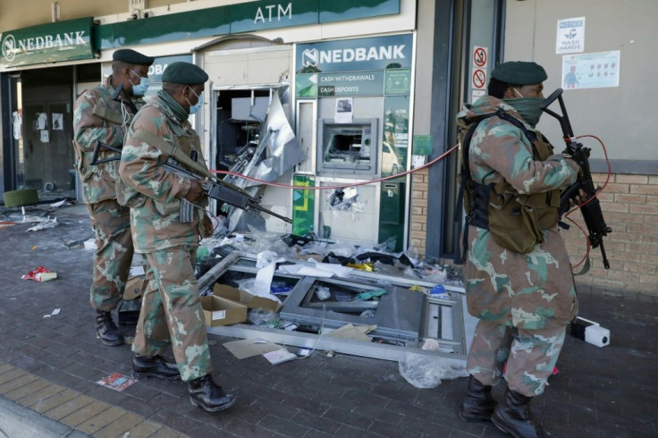 Troops walk past the remains of an automated teller machine (ATM) in the Diepkloof Square mall in Soweto