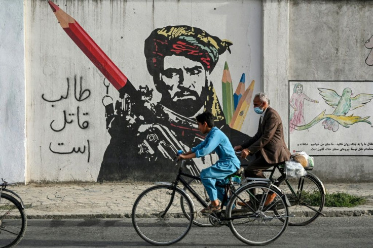Cyclists peddle past a mural painted on the wall along a road in Kabul