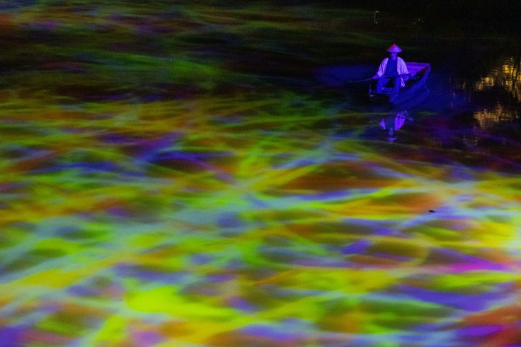 On the surface of a pond, abstract lines of violet, yellow and green light combine
