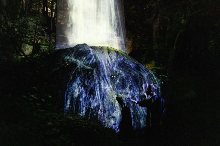 A cascading waterfall made entirely of light pours onto a rock