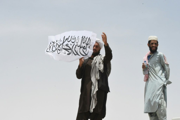 A man standing on Afghanistan's side of the border holds a Taliban flag as people walk towards a border crossing point in Pakistan