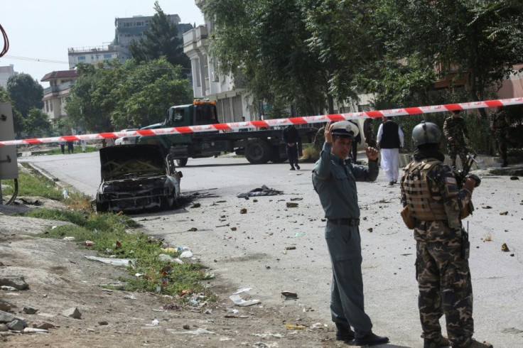 Afghan security personnel stand guard near a charred vehicle from which rockets were fired that landed near the Afghan presidential palace in Kabul