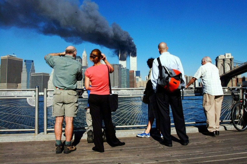 Pedestrians standing on the Brooklyn waterfront look across the East River towards the burning Twin Towers of the World Trade Center in lower Manhattan, New York on September 11, 2001