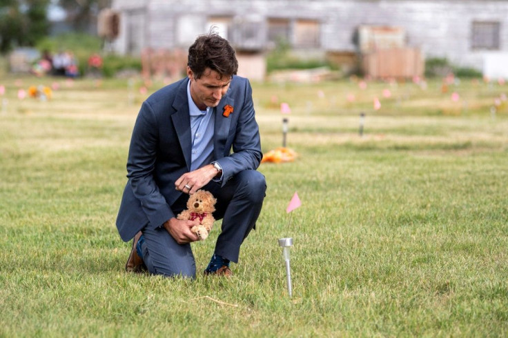 Prime Minister Justin Trudeau lays a teddy bear at a small flag in a field prior to a ceremony at the site of a former residential school on July 6, 2021