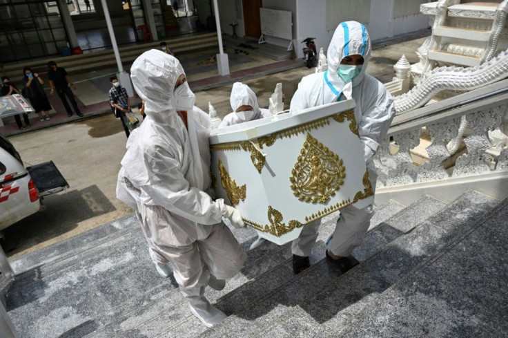 The family of Malee Manjeen, who passed away due to Covid-19, watch from a distance as monks in personal protective equipment carry her coffin to the crematorium