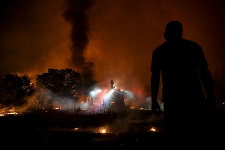 A person watches a fire fighter dousing flames from the top of a truck as a fire spreads around the village of Afidnes, some 30 kilometres north of Athens