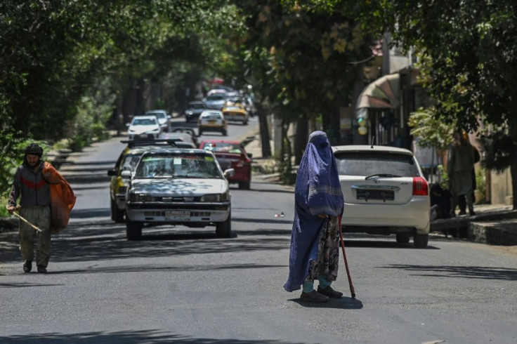 A burqa clad woman seeks money from drivers as she stands in the middle of a road in Kabul on August 6, 2021