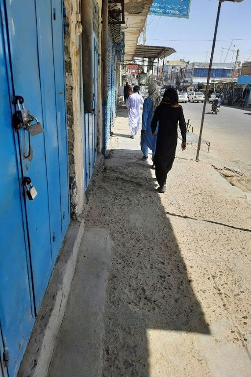 Afghan men walk past closed shops along a road in Zaranj, a day after the city fell to the Taliban