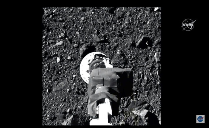 A NASA video frame handout image shows the robotic arm from NASA spacecraft OSIRIS-REx collecting samples from the asteroid Bennu