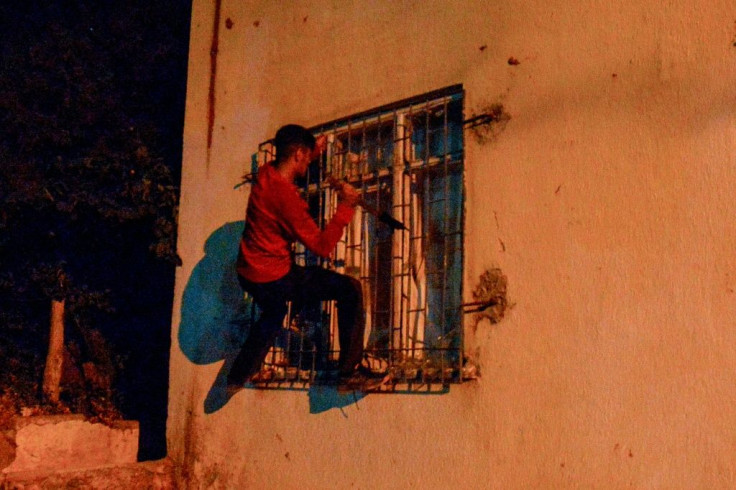 A young man trying to break into the apartment of a building by dislodging the metal wiring of its ground floor window