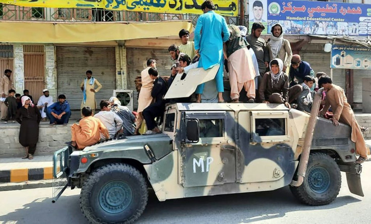 Taliban fighters and local residents sit on a captured Afghan National Army humvee vehicle in Laghman province