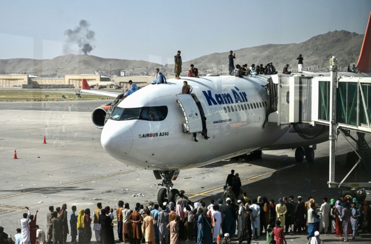Afghan people climb atop a plane as they wait at the Kabul airport after a stunningly swift end to Afghanistan's 20-year war, as thousands of people mobbed the city's airport trying to flee the group's feared hardline brand of Islamist rule