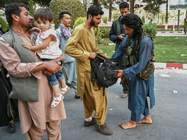 A Taliban fighter (R) searches the bags of people coming out of the Kabul airport