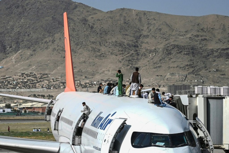 Afghans climb atop a plane at the Kabul airport on August 16, 2021, as hundreds of people mobbed the facility, clinging to planes even as they taxiied down the runway in an attempt to flee Taliban rule