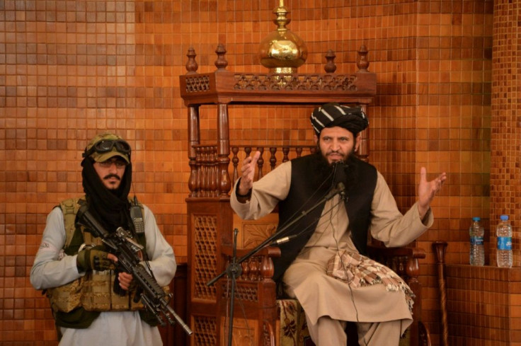 An imam speaks next to an armed Taliban fighter during Friday prayers at the Abdul Rahman Mosque in Kabul on August 20, 2021, following the Taliban's stunning takeover of Afghanistan