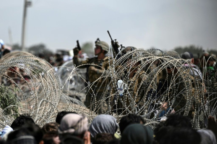A US soldier shoots in the air with his pistol while standing guard behind barbed wire as Afghans sit on a roadside near the military part of the airport in Kabul