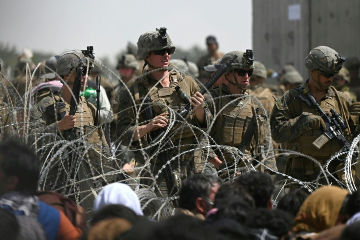 US soldiers stand guard behind barbed wire as Afghans sit on a roadside near the military part of the airport in Kabul on August 20, 2021, hoping to flee from the country