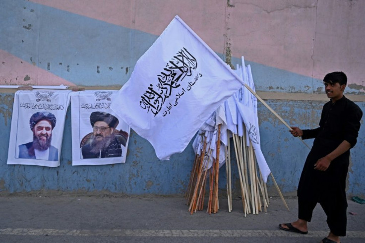 A vendor holds a Taliban flag next to posters of Taliban leaders Mullah Abdul Ghani Baradar and Amir Khan Muttaqi (L) as he waits for customers along a street in Kabul