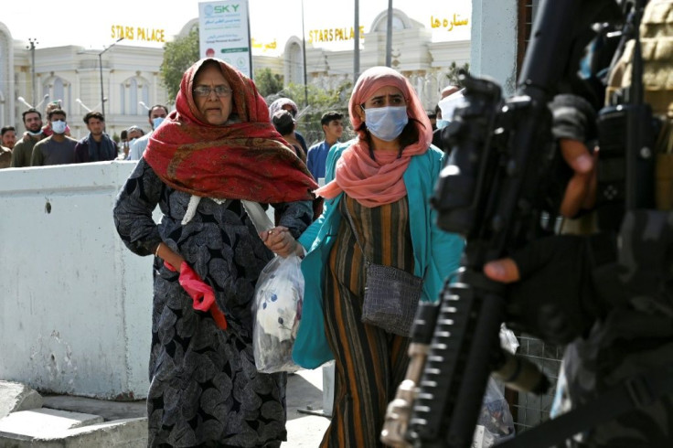 Taliban fighters stand guard as Afghans hoping to leave the country walk through the main entrance of Kabul airport