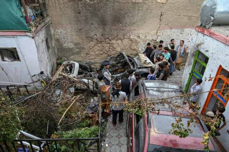 Afghan residents and family members of the victims gather next to a damaged vehicle inside a house, after a US drone strike which they say went wrong in Kabul