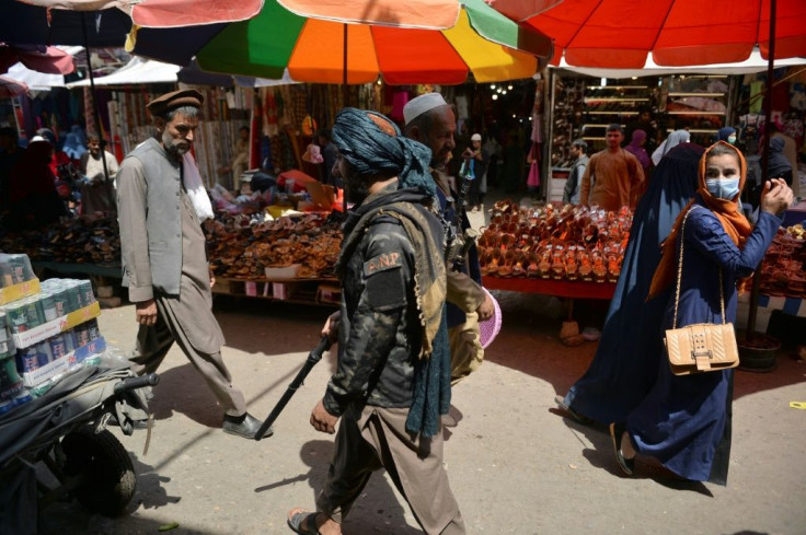 A woman looks back as a Taliban fighter (C) walks past shoppers along Mandawi market in Kabul on September 1, 2021