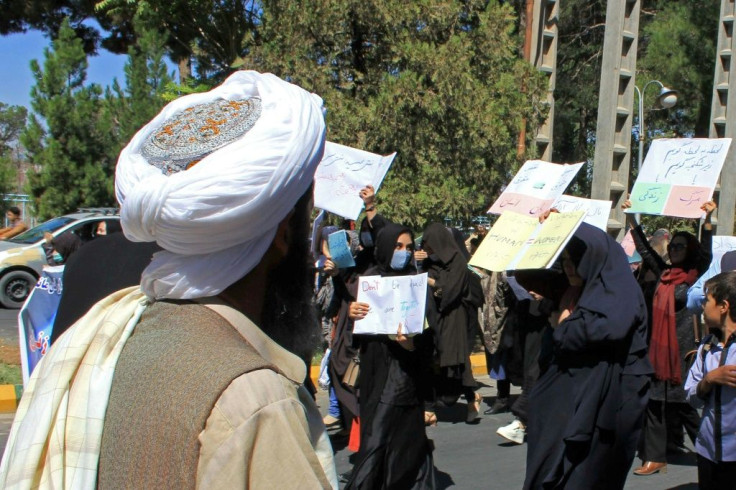 A member (L) of the Taliban watches as Afghan women hold placards demanding their rights during a rare protest in Herat on September 2, 2021