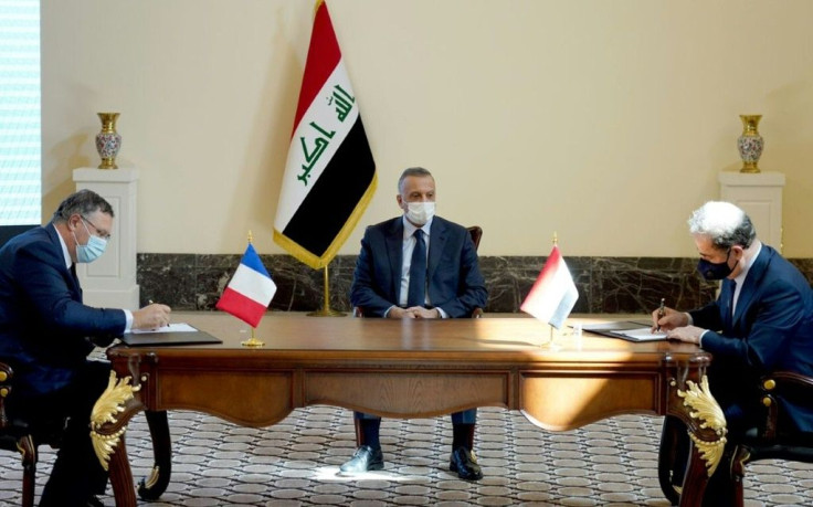 A representative of the Iraqi government (R) and TotalEnergies chief Patrick Pouyanne (L) sign the contract in the presence of Iraqi Prime Minister Mustafa al-Kadhemi in the capital Baghdad