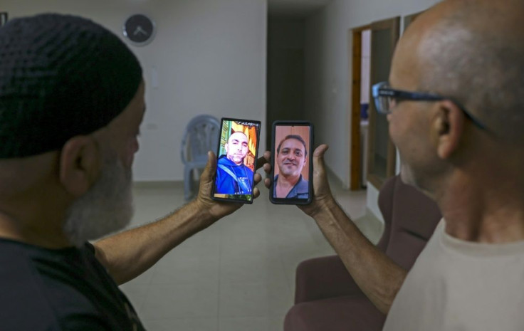 Malek Hassuna, left, holds up his phone with a picture of his late son Mussa, and Effi Yehoshua shows a photo of his late brother Yigal