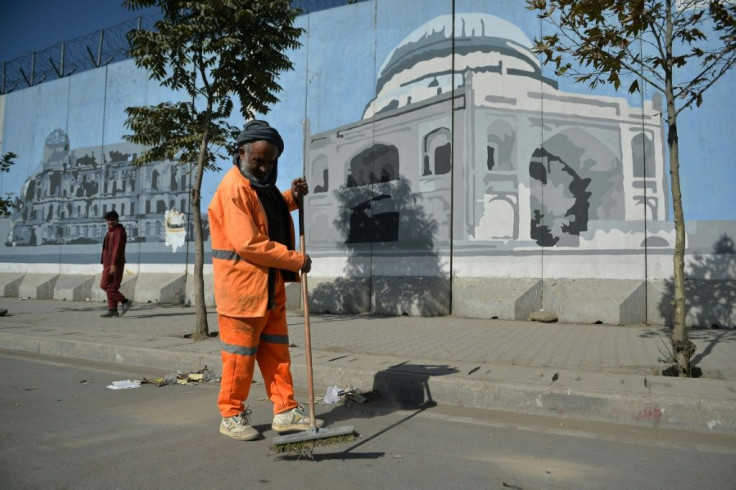 An Afghan worker cleans a road next to a mural in Kabul