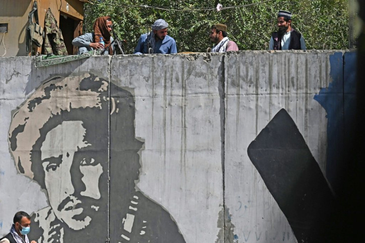 Taliban fighters by a concrete wall painted with an image of Ahmad Shah Massoud