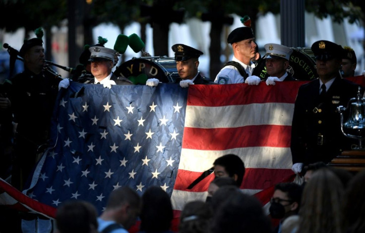 New York police and firefighters hold a US flag as a band plays the US National Anthem at the National 9/11 Memorial during a ceremony commemorating  the 20th anniversary of the attacks