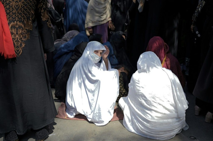 Women wait in front of a bank to withdraw money in Kabul