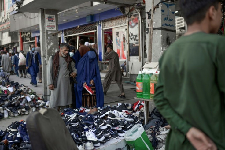 A burqa-clad woman checks footwear displayed on a stall at a market area in Kabul