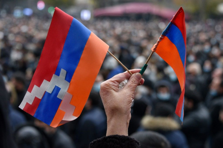 A woman holds a flag (L) of the breakaway Nagorno-Karabakh region and an Armenian flag (R) during a rally against a controversial peace agreement with Azerbaijan in Yerevan on December 5, 2020