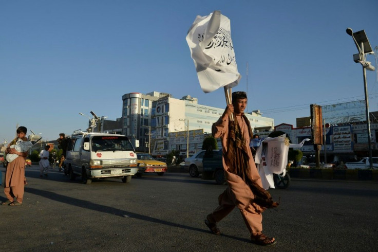 A boy selling Taliban flags looks for customers while walking along a road in Herat
